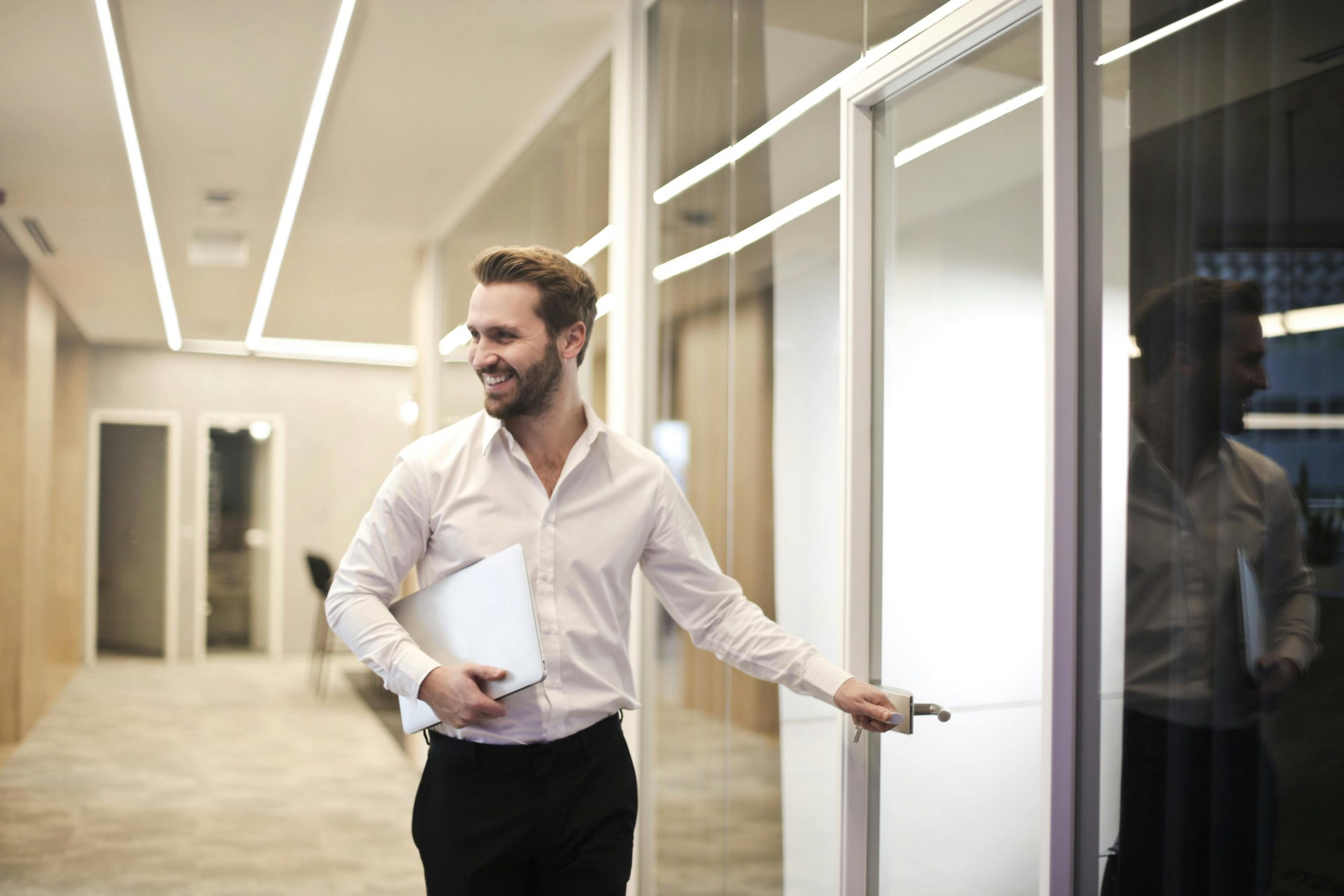 professionally dressed man holding documents and opening a glass office door